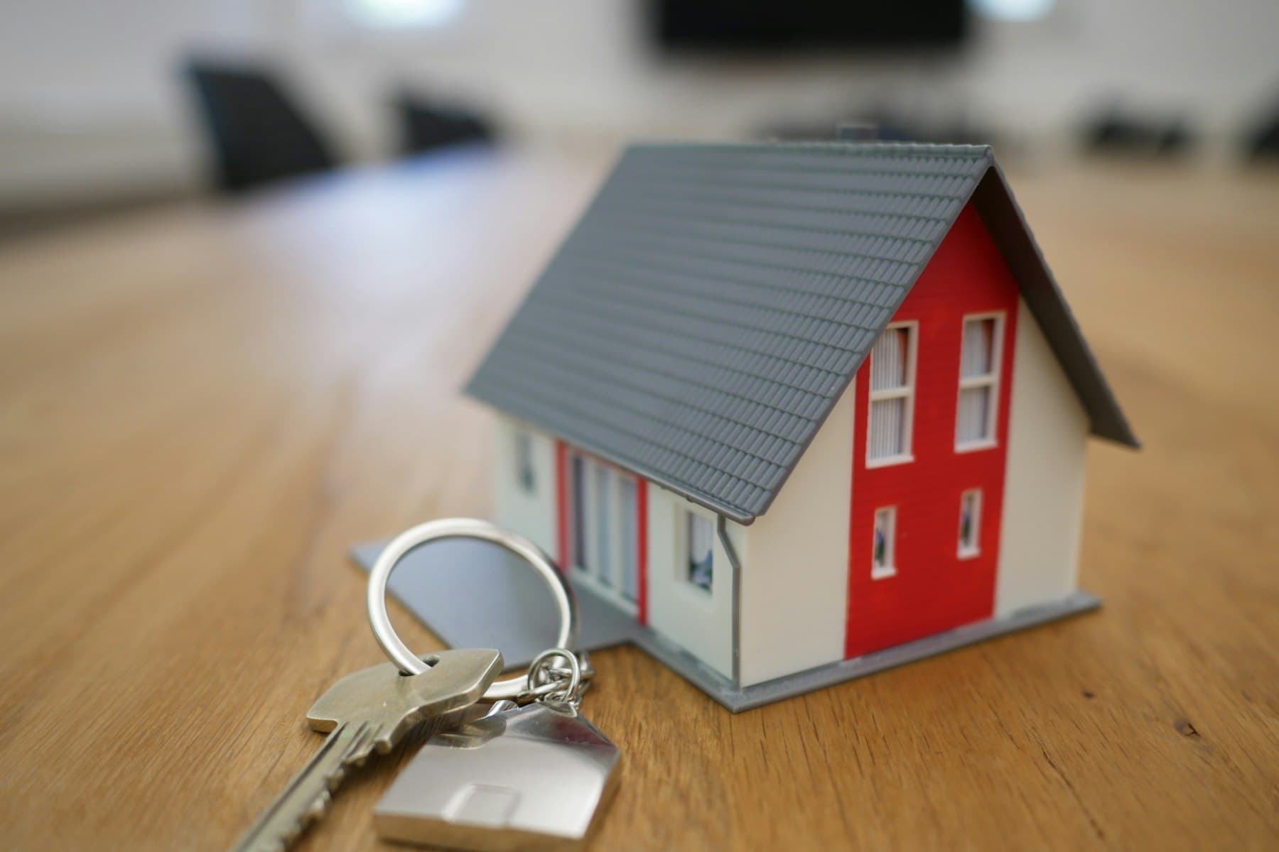 A small model house and a set of keys on a wooden table.